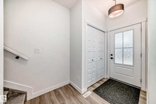 Entryway featuring wood-finish flooring, a contemporary pendant light fixture, a paneled front door with decorative glass, and bi-fold closet doors - 38 1910 Collip View, Edmonton, AB - Indoor Photo Showing Other Room