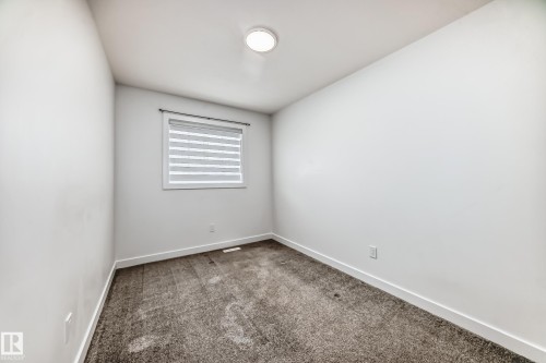 Neutral wall finishes, textured carpeting, contemporary ceiling light fixture, and window with horizontal blinds - 38 1910 Collip View, Edmonton, AB - Indoor Photo Showing Other Room