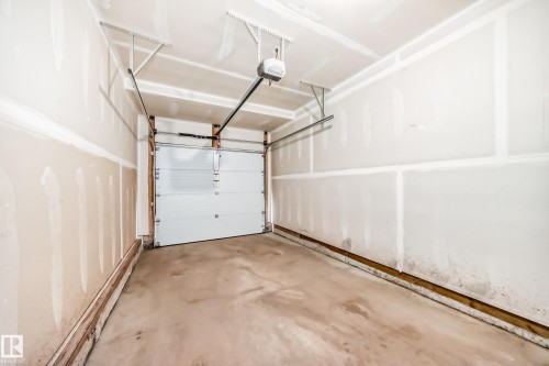 Single-car garage featuring a concrete floor, an automatic garage door opener system, and unfinished drywall walls and ceiling - 38 1910 Collip View, Edmonton, AB - Indoor Photo Showing Garage
