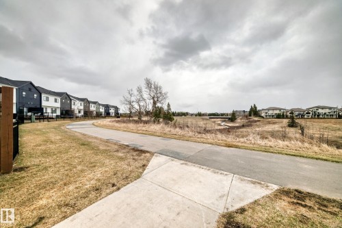 Paved pathway bordered by manicured lawn and mature trees, featuring a distant bridge structure - 38 1910 Collip View, Edmonton, AB - Outdoor With View