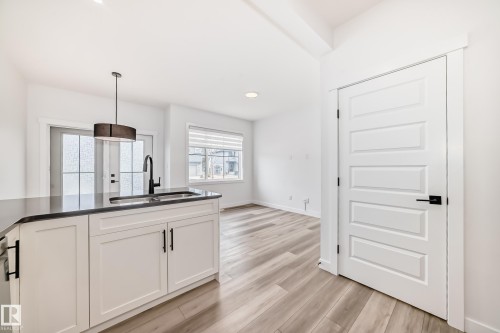 Kitchen island with a dark countertop and white cabinetry featuring a stainless steel sink and matte black faucet - 38 1910 Collip View, Edmonton, AB - Indoor