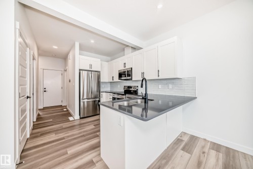 Modern kitchen featuring white shaker cabinetry, stainless steel appliances, dark countertops, and a subway tile backsplash - 38 1910 Collip View, Edmonton, AB - Indoor Photo Showing Kitchen