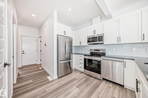 Kitchen featuring white cabinetry, stainless steel appliances, dark countertops, a light-toned tile backsplash, and wood-finish flooring - 38 1910 Collip View, Edmonton, AB - Indoor Photo Showing Kitchen With Upgraded Kitchen