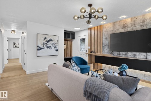 Living area featuring a modern chandelier, wood-finish flooring, recessed lighting, a stone-accented wall, and a custom built-in entertainment console with accent lighting - 13332 106 Street, Edmonton, AB - Indoor Photo Showing Living Room