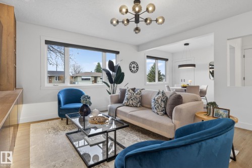 Open-concept living area featuring wood-finish flooring, a contemporary chandelier, large windows with black roller shades, and a built-in media console - 13332 106 Street, Edmonton, AB - Indoor Photo Showing Living Room