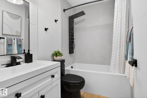 Bathroom featuring a white vanity with matte black hardware, a black toilet, a tub with a black shower system, and light-toned tile flooring - 13332 106 Street, Edmonton, AB - Indoor Photo Showing Bathroom