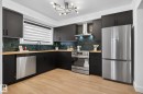 Modern kitchen featuring dark cabinetry, wood-finish countertops, stainless steel appliances, a textured tile backsplash, and light wood-finish flooring - 13332 106 Street, Edmonton, AB  - Indoor Photo Showing Kitchen 
