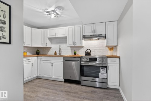 Kitchen featuring white cabinetry, wood-finish countertops, stainless steel appliances, white subway tile backsplash, and wood-finish flooring - 13332 106 Street, Edmonton, AB - Indoor Photo Showing Kitchen