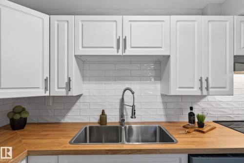 Kitchen featuring bright white shaker-style cabinetry, a subway tile backsplash, wood-finish countertops, and a stainless steel double basin sink with a gooseneck faucet - 13332 106 Street, Edmonton, AB - Indoor Photo Showing Kitchen With Double Sink