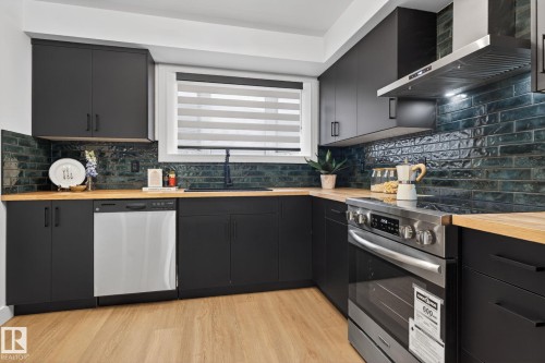 Contemporary kitchen featuring dark cabinetry, wood-finish countertops, and a textured green subway tile backsplash - 13332 106 Street, Edmonton, AB - Indoor Photo Showing Kitchen