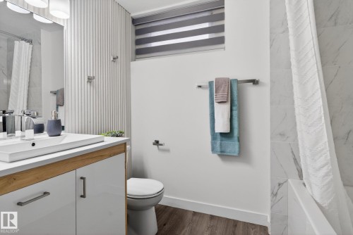 Contemporary bathroom featuring a vanity with a rectangular integrated sink, wood-finish base, and white cabinetry - 13332 106 Street, Edmonton, AB - Indoor Photo Showing Bathroom