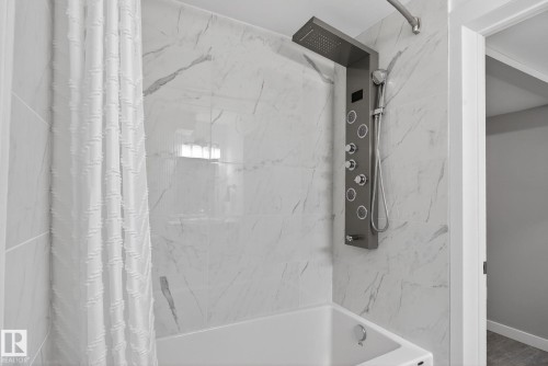 Bathroom featuring a white bathtub, large format marble-look wall tiles, and a multi-function shower panel with an integrated rain shower and handheld sprayer - 13332 106 Street, Edmonton, AB - Indoor Photo Showing Bathroom