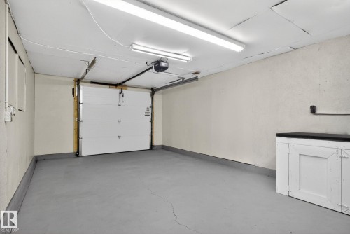 Attached garage with a white sectional door, gray concrete flooring, and an overhead lighting fixture - 13332 106 Street, Edmonton, AB - Indoor Photo Showing Garage