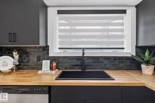 Kitchen featuring a window with layered blinds, dark cabinetry, wood-finish countertops, black sink, and black faucet - 13332 106 Street, Edmonton, AB - Indoor Photo Showing Kitchen