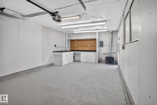 Spacious garage featuring concrete flooring, built-in cabinetry with dark countertops, and fluorescent ceiling lighting - 13332 106 Street, Edmonton, AB - Indoor Photo Showing Garage