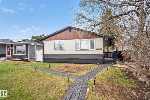 Front exterior featuring a covered entry, dark wood-tone siding, light stucco finish, and a stone paver pathway - 13332 106 Street, Edmonton, AB - Outdoor