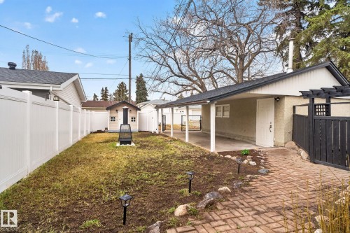 Expansive backyard featuring a white privacy fence, detached shed, and a brick paver pathway leading to a covered patio - 13332 106 Street, Edmonton, AB - Outdoor