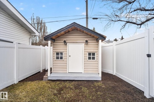 Detached shed with beige siding, a dark roof, and a small front porch, framed by white privacy fencing - 13332 106 Street, Edmonton, AB - Outdoor