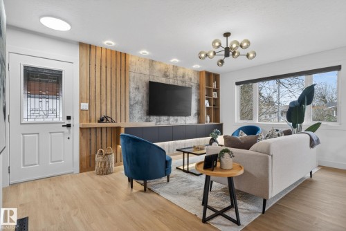 Open-concept living area featuring wood-finish flooring, a contemporary chandelier, recessed ceiling lighting, a large picture window with roller shades, and a built-in media console with integrated shelving and accent lighting - 13332 106 Street, Edmonton, AB - Indoor Photo Showing Other Room