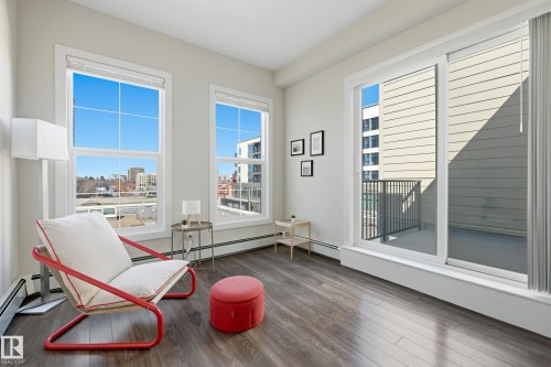 Spacious room with large windows, wood-finish flooring, and a sliding glass door leading to a private balcony with metal railings - 403 10418 81 Avenue, Edmonton, AB - 