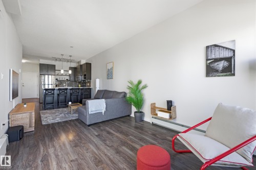 Open-concept living area featuring wood-finish flooring, a contemporary kitchen with dark cabinetry and stainless steel appliances, and a breakfast bar with pendant lighting - 403 10418 81 Avenue, Edmonton, AB - Indoor Photo Showing Living Room