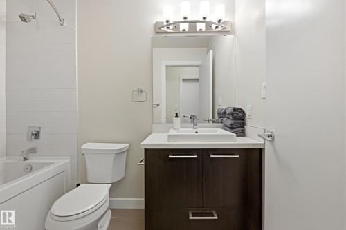 Contemporary bathroom featuring a dark wood-finish vanity with a vessel sink, a full-width mirror, and a three-light fixture - 403 10418 81 Avenue, Edmonton, AB - Indoor Photo Showing Bathroom