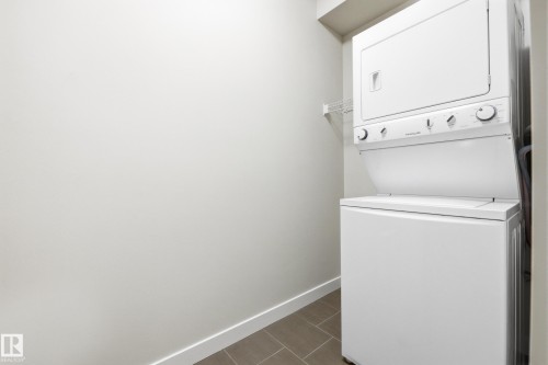 Integrated laundry center featuring a stacked washer and dryer, tile flooring, and white walls - 403 10418 81 Avenue, Edmonton, AB - Indoor Photo Showing Laundry Room