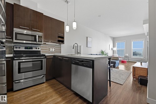 Kitchen featuring stainless steel appliances, dark wood-finish cabinetry, light countertops, and wood-finish flooring - 403 10418 81 Avenue, Edmonton, AB - Indoor Photo Showing Kitchen With Upgraded Kitchen