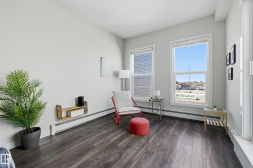 Bright room featuring two large windows, wood-finish flooring, white baseboards, and a built-in wall shelf - 403 10418 81 Avenue, Edmonton, AB - Indoor