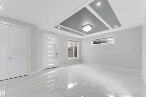 Spacious interior featuring large format tile flooring and a tray ceiling with recessed lighting and a central chandelier - 3736 1 Avenue Sw, Edmonton, AB - Indoor Photo Showing Other Room