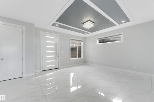 Spacious entry area featuring large format tile flooring, a modern front door with vertical lites, a recessed tray ceiling with accent lighting, and multiple windows providing natural light - 3736 1 Avenue Sw, Edmonton, AB - Indoor Photo Showing Other Room