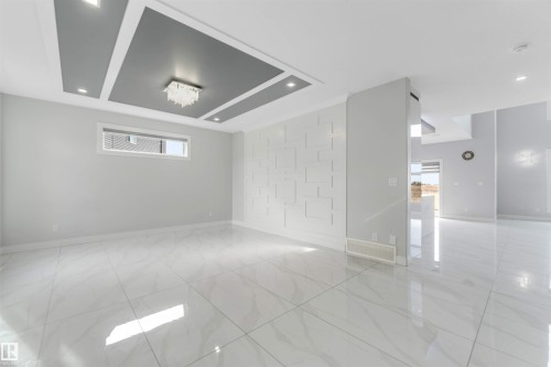 Spacious interior featuring large format tile flooring, a decorative accent wall, and a tray ceiling with integrated lighting - 3736 1 Avenue Sw, Edmonton, AB - Indoor Photo Showing Other Room