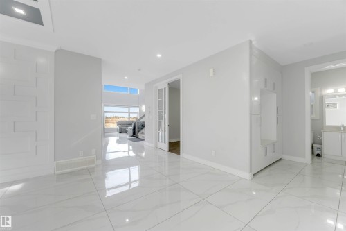 Spacious interior featuring large format marble-look tile flooring, recessed lighting, and a modern built-in shelving unit - 3736 1 Avenue Sw, Edmonton, AB - Indoor Photo Showing Other Room