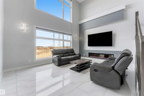 Double-height living space featuring large format tile flooring, a wall-mounted linear fireplace, and expansive windows - 3736 1 Avenue Sw, Edmonton, AB - Indoor Photo Showing Living Room With Fireplace