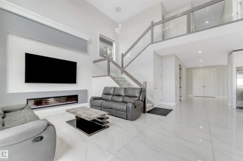 Two-story living area featuring a built-in linear electric fireplace, high ceilings, white tile flooring, and a glass-paneled staircase with a matching second-story railing - 3736 1 Avenue Sw, Edmonton, AB - Indoor Photo Showing Living Room With Fireplace