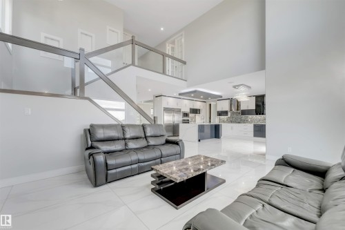 Two-story living area featuring a glass and metal staircase, high ceilings, large format tile flooring, and open sightlines to a contemporary kitchen with modern cabinetry - 3736 1 Avenue Sw, Edmonton, AB - Indoor Photo Showing Living Room