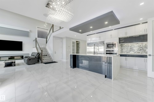 Open-concept living space featuring high-gloss white tile flooring, a contemporary kitchen island with a quartz countertop, stainless steel appliances, and a built-in electric fireplace - 3736 1 Avenue Sw, Edmonton, AB - Indoor Photo Showing Kitchen With Upgraded Kitchen