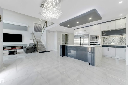 Open-concept living space featuring sleek tile flooring, a modern kitchen island with integrated sink, stainless steel appliances, and a contemporary fireplace - 3736 1 Avenue Sw, Edmonton, AB - Indoor Photo Showing Kitchen With Upgraded Kitchen