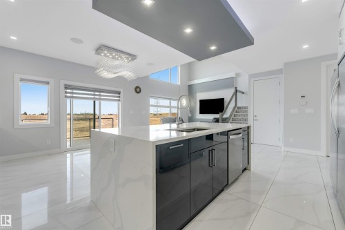Kitchen island with integrated sink, white quartz waterfall countertop, dark cabinetry, and a built-in dishwasher - 3736 1 Avenue Sw, Edmonton, AB - Indoor Photo Showing Kitchen With Double Sink