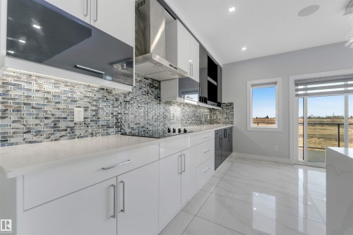 Modern kitchen featuring white and dark gray cabinetry, a mosaic tile backsplash, white countertops, an integrated cooktop, and large format polished floor tiles - 3736 1 Avenue Sw, Edmonton, AB - Indoor Photo Showing Kitchen With Upgraded Kitchen