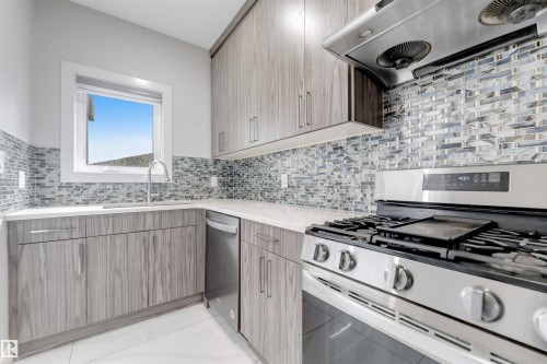 Contemporary kitchen featuring wood-finish cabinetry, light-toned countertops, and a patterned tile backsplash - 3736 1 Avenue Sw, Edmonton, AB - Indoor Photo Showing Kitchen With Upgraded Kitchen