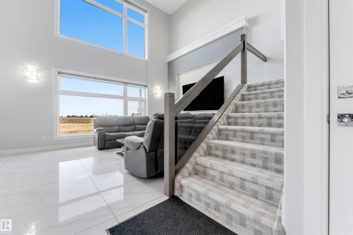 Two-story living area featuring high ceilings, expansive windows, a modern glass and wood-finish staircase with patterned carpeting, and polished tile flooring - 3736 1 Avenue Sw, Edmonton, AB - Indoor Photo Showing Other Room