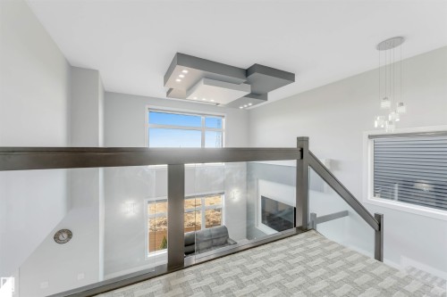 Upper-level landing featuring a glass and wood-finish railing, patterned carpet, and a modern tiered ceiling fixture with integrated lighting - 3736 1 Avenue Sw, Edmonton, AB - Indoor Photo Showing Other Room