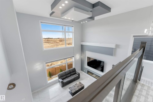 Two-story living area featuring large picture windows, a modern fireplace, ceiling architectural details, and light tile flooring - 3736 1 Avenue Sw, Edmonton, AB - Indoor With Fireplace