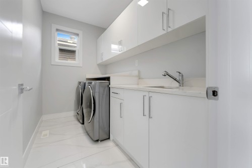 Dedicated laundry area featuring white flat-panel cabinetry, a stainless steel sink, and light-toned countertops - 3736 1 Avenue Sw, Edmonton, AB - Indoor Photo Showing Laundry Room