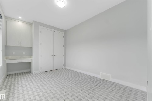 Built-in desk area with upper cabinetry and a light-toned countertop, featuring a patterned carpet and double-door closet - 3736 1 Avenue Sw, Edmonton, AB - Indoor Photo Showing Other Room