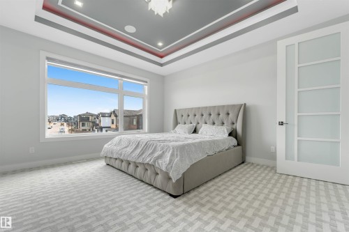 Spacious room featuring a large window, patterned carpeting, a multi-tiered tray ceiling with recessed lighting, and a modern interior door with frosted glass panels - 3736 1 Avenue Sw, Edmonton, AB - Indoor Photo Showing Bedroom