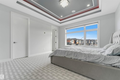 Recessed tray ceiling with accent lighting, large picture window, patterned carpet flooring, modern white doors, and contemporary light fixtures - 3736 1 Avenue Sw, Edmonton, AB - Indoor Photo Showing Bedroom