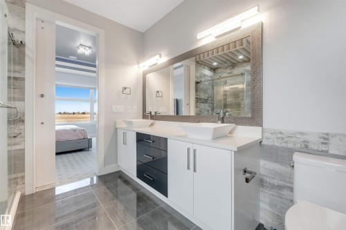 Contemporary bathroom featuring dual vessel sinks on a white countertop with a two-tone vanity, large framed mirror with integrated lighting, and a tiled shower enclosure - 3736 1 Avenue Sw, Edmonton, AB - Indoor Photo Showing Bathroom