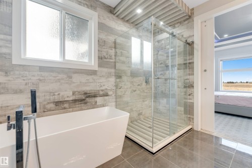 Bathroom featuring a freestanding soaking tub with floor-mounted faucet, glass-enclosed shower, and wood-finish tile wall accents - 3736 1 Avenue Sw, Edmonton, AB - Indoor Photo Showing Bathroom